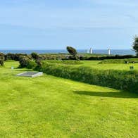Golf green and trees with the ocean and a blue sky in the background