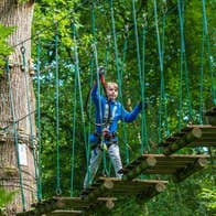 Boy walking across a rope bridge wearing a harness at Zipit Lough Key Ltd, Roscommon