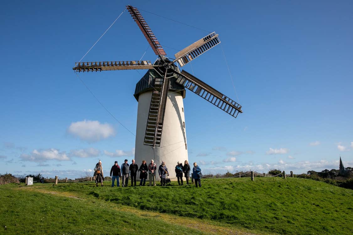 A group of people posing outside a windmill with five sails