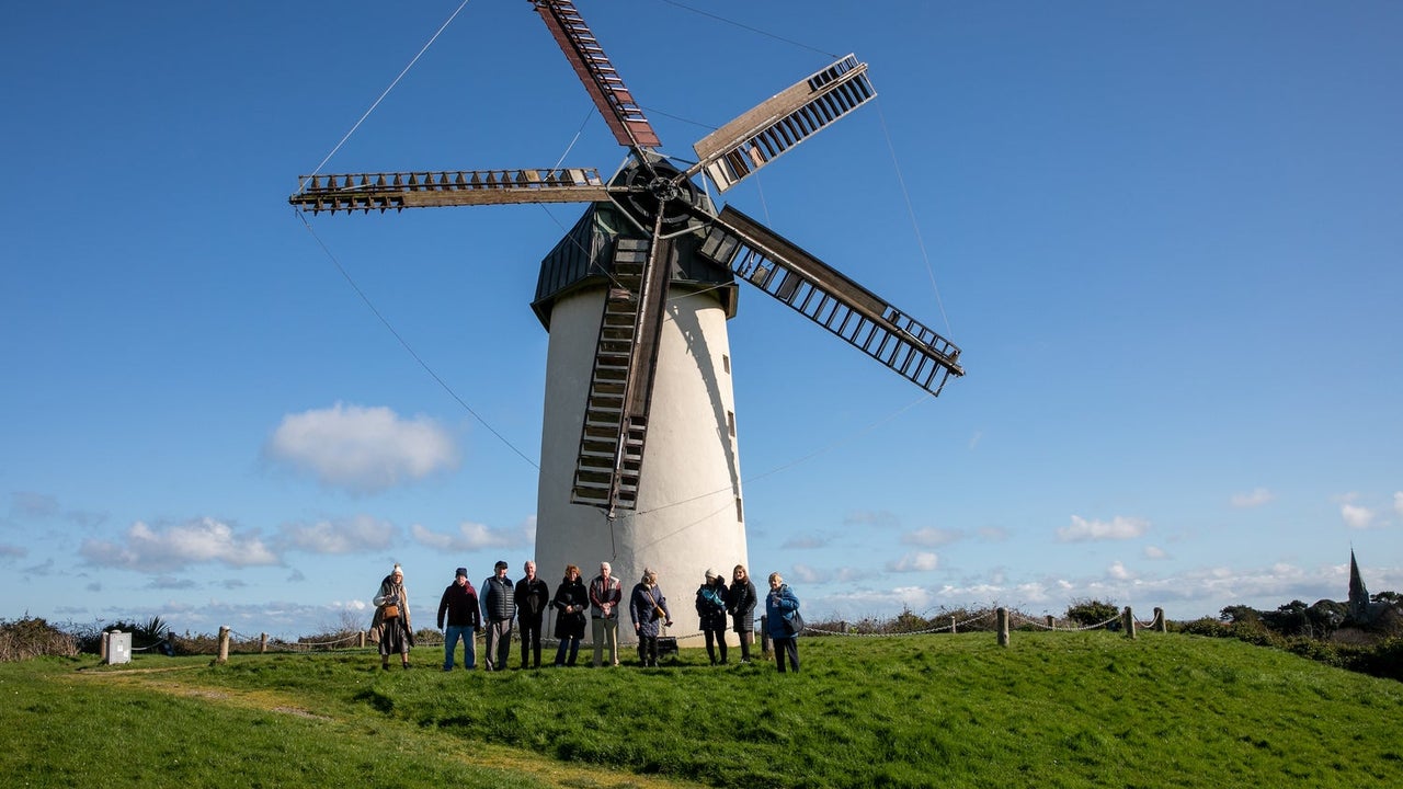 A group of people posing outside a windmill with five sails