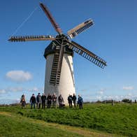 A group of people posing outside a windmill with five sails
