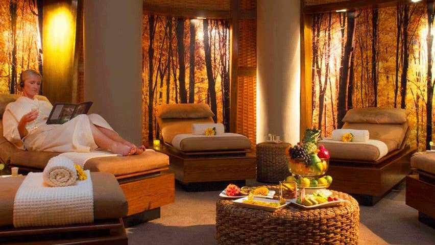 A lady in a bathrobe relaxing on a lounge in a softly lit room in the Escape Spa at the Imperial Hotel