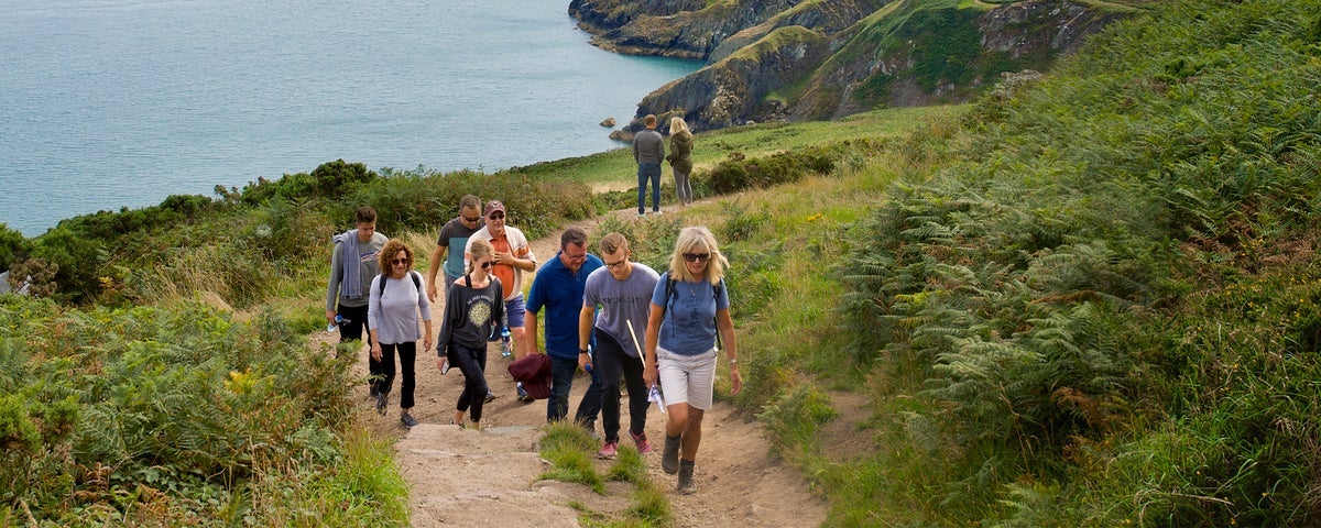 Group of people walking along a coastal path with the sea in the background