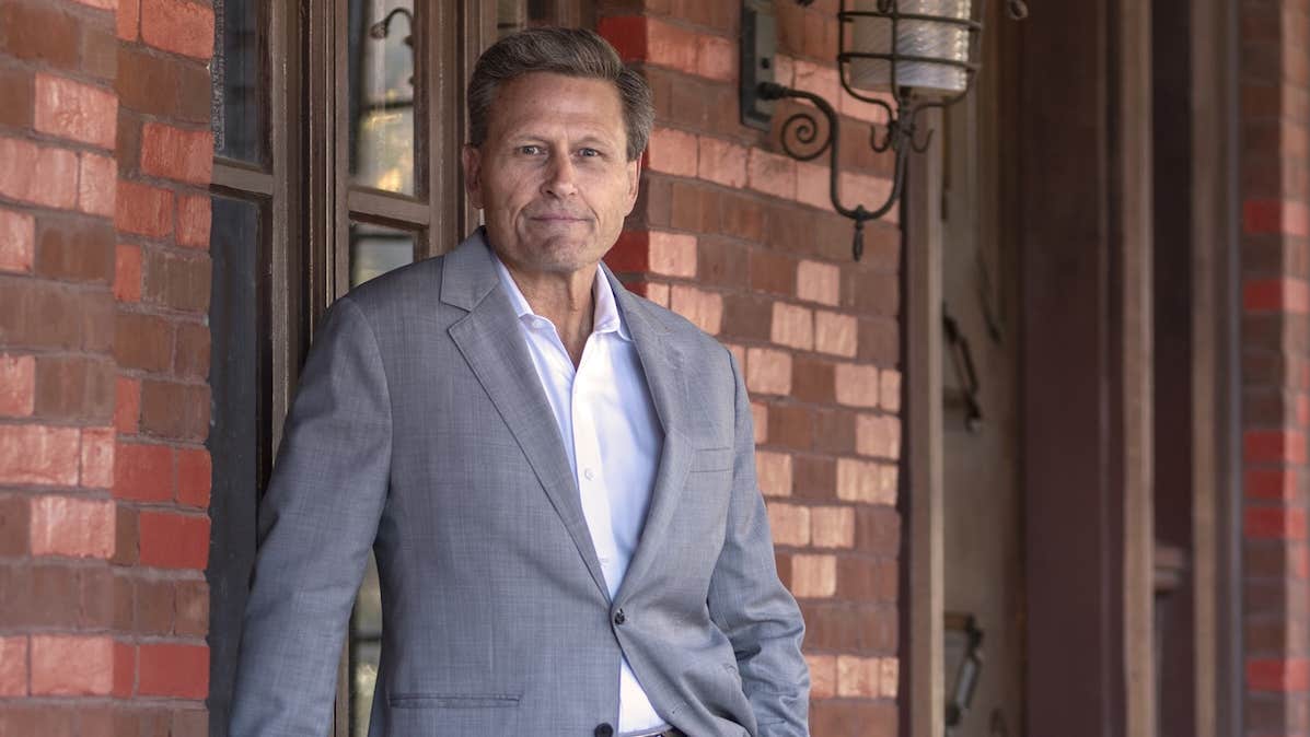 A slightly smiling man in grey jacket in front of a brick building