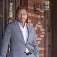 A slightly smiling man in grey jacket in front of a brick building