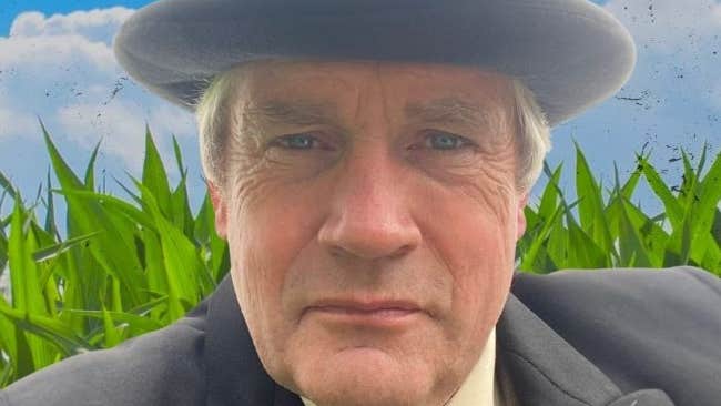 The Love Hungry Farmer by John B Keane, a man in grey hat and suit and tie with green grass and blue sky in background.