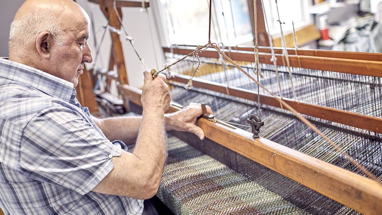 Man sitting at a loom weaving wool