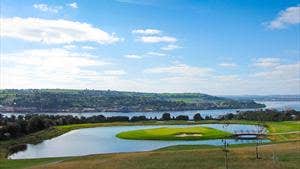 View of a golf course beside a water feature with the coast in the distance