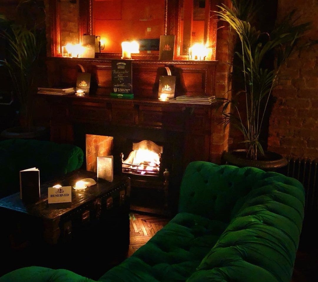 A plush dark green couch next to a blazing fire in Idlewild Pub in Dublin city.
