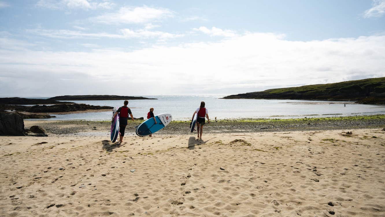 Three paddle boarders on the sand on their way into the sea