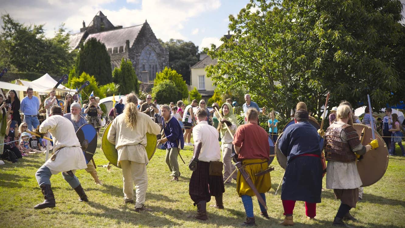 Men dressed in medieval clothes with weapons in mock battle watched by a crowd.