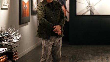 The artist poses for a photograph in front of his work inside a gallery
