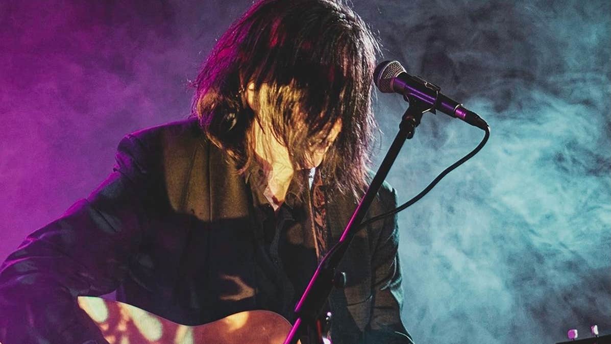 A man playing guitar with his face obscured by his long hair