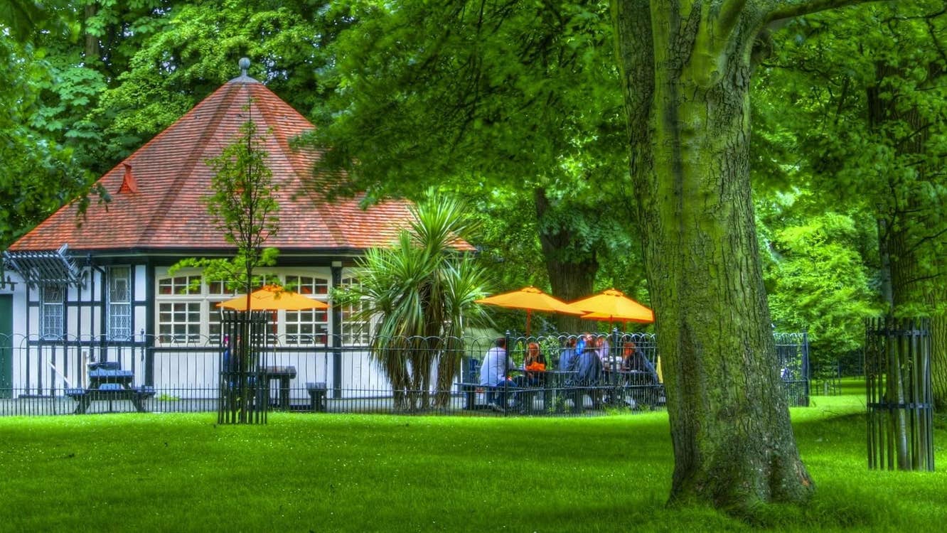Exterior of a tea room with an outside seating set on parkland surrounded by trees