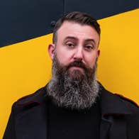 A man with long beard standing against bright yellow wall