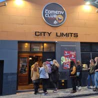 A group of people waiting outside a grey and yellow building.