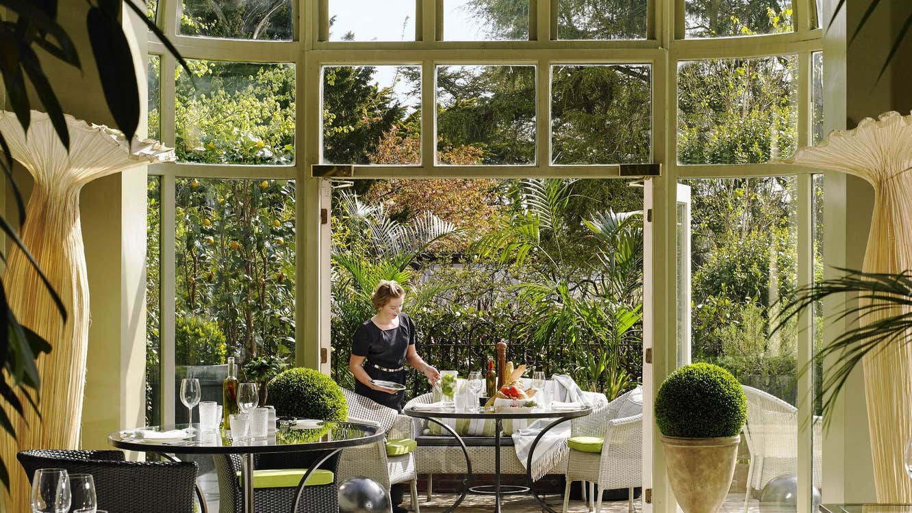 Garden view restaurant with a staff member setting a table beside large open windows