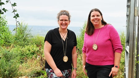 Two ladies posing with smiles with hills in the background
