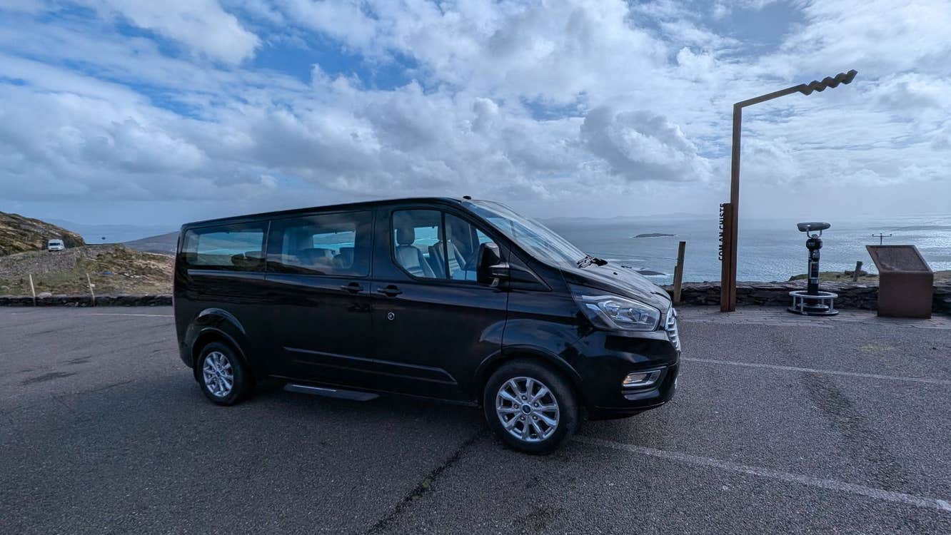 Black chauffeur minibus parked at a scenic coastal viewpoint