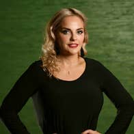 A gently smiling woman in black top with dark green background.