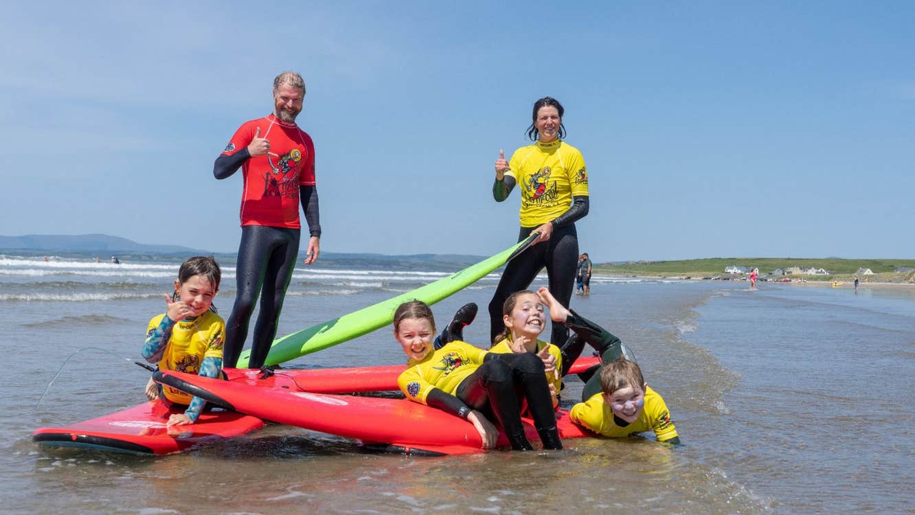 Surf instructors and children in wetsuits on the beach with red and green surfboards