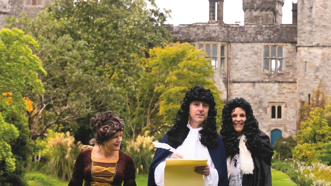 Robert Boyle Summer School 2026, 2 men in curly dark wigs and costumes and woman in big dress, outdoors with castle in background.