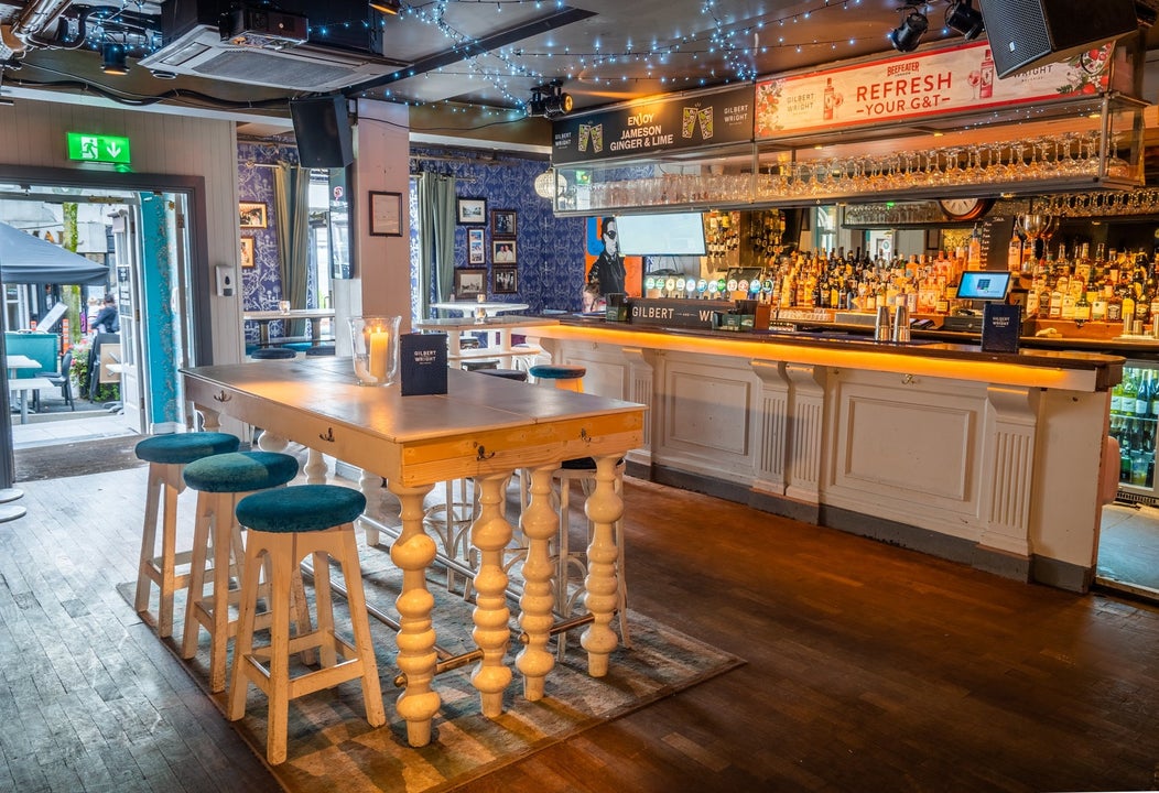 Interior of a bar with a wooden floor tall white table and three high stools