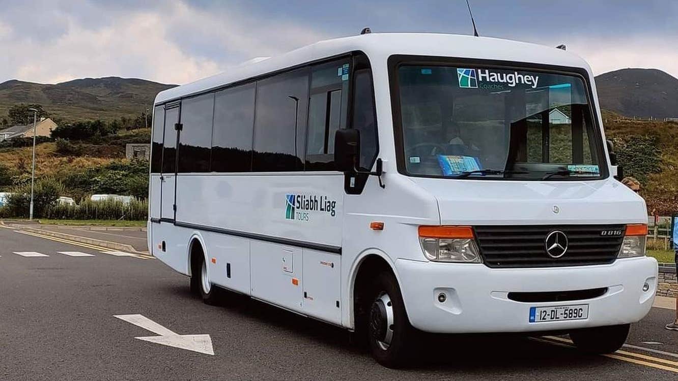 A minibus with a tour company logo parked in a scenic location