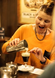 A woman pouring cream onto a brown liquid in a cocktail glass