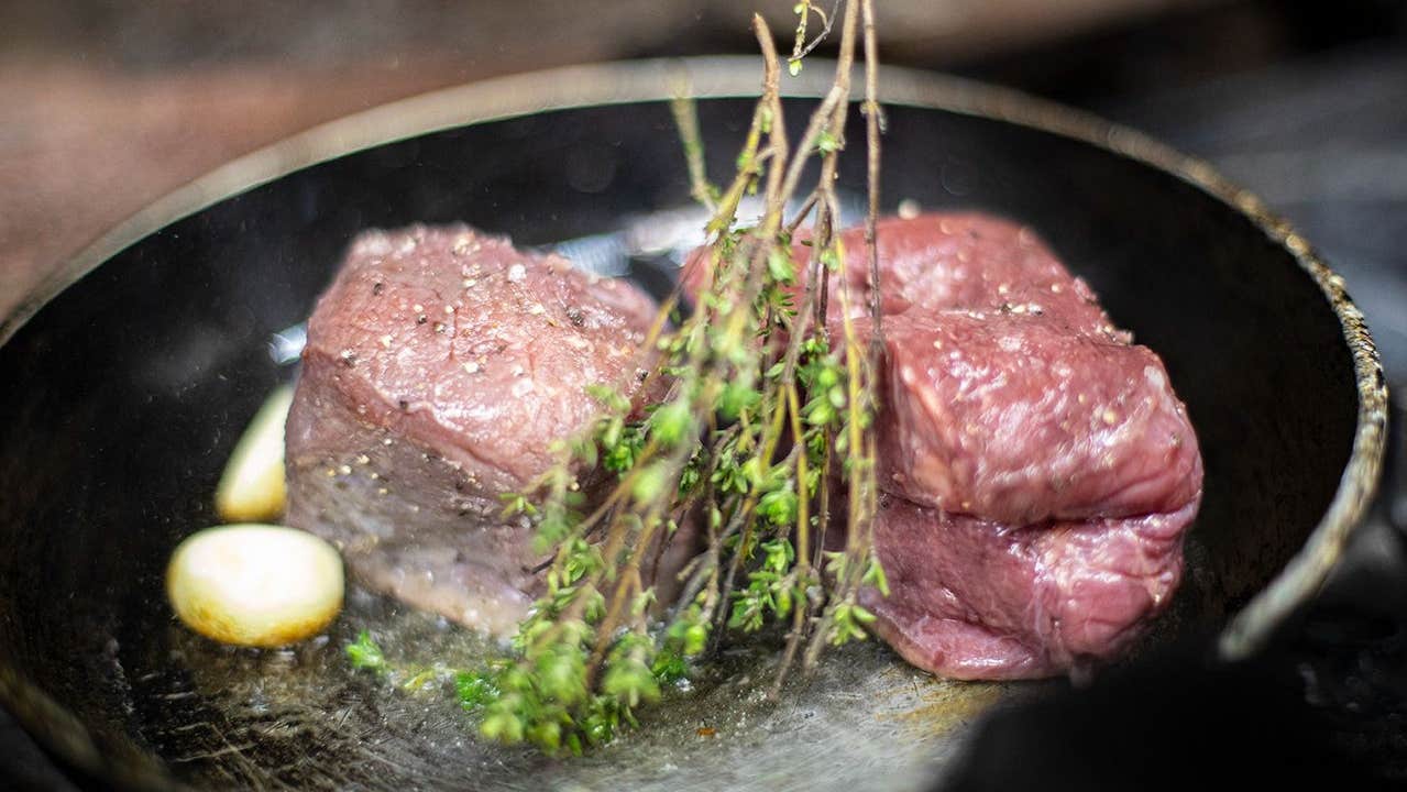 Two steaks with garlic and herbs in a hot pan