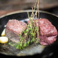 Two steaks with garlic and herbs in a hot pan