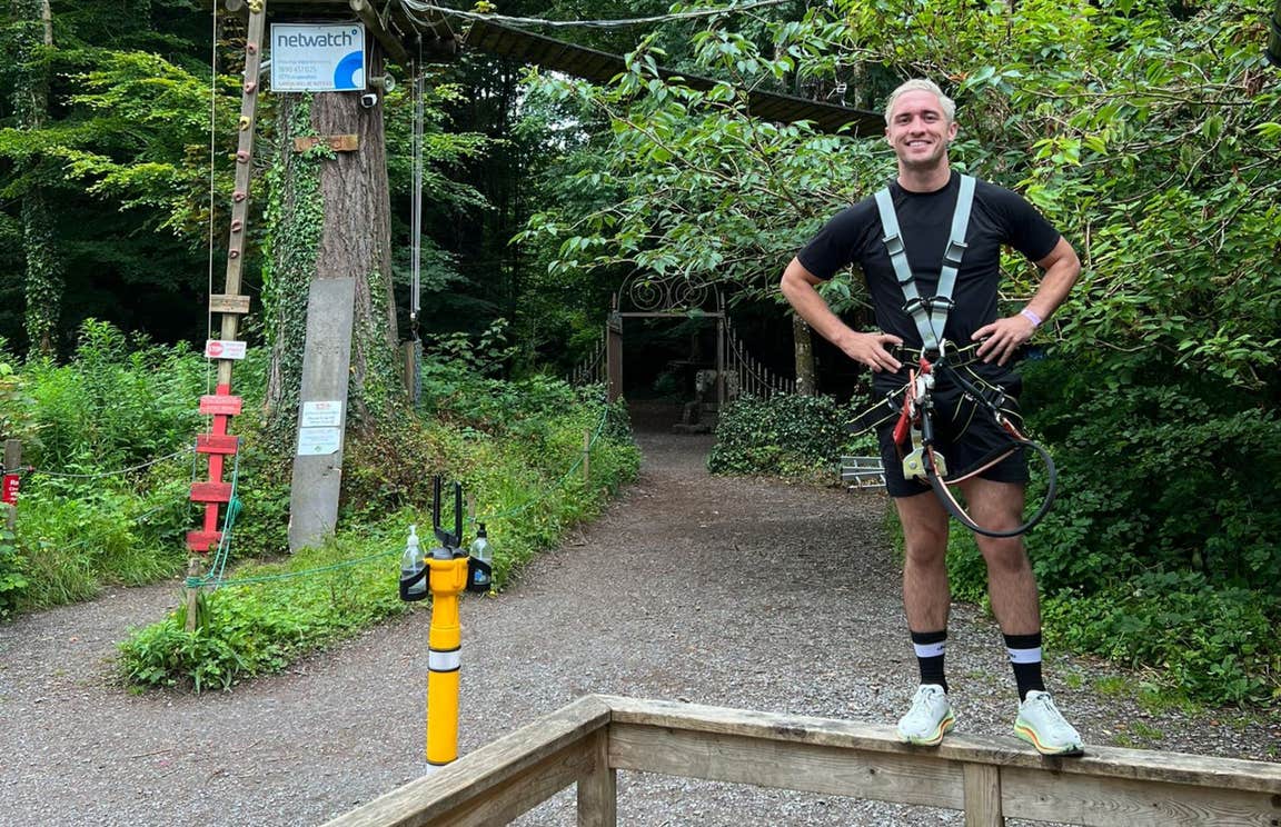 Man standing on a low fence in front of an adventure park.