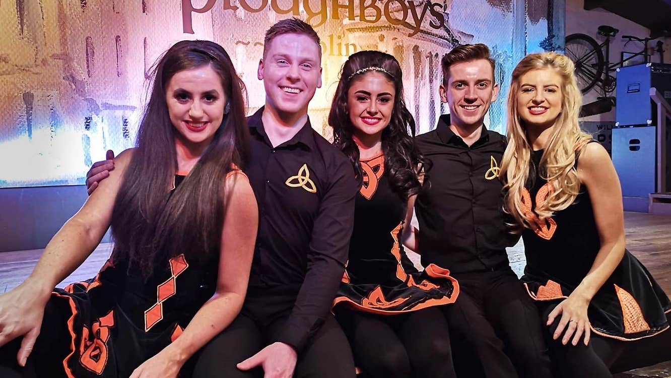 Five Irish dancers sit on a stage to pose for a photograph