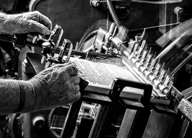 Black and white photo of hands operating old printing machine.
