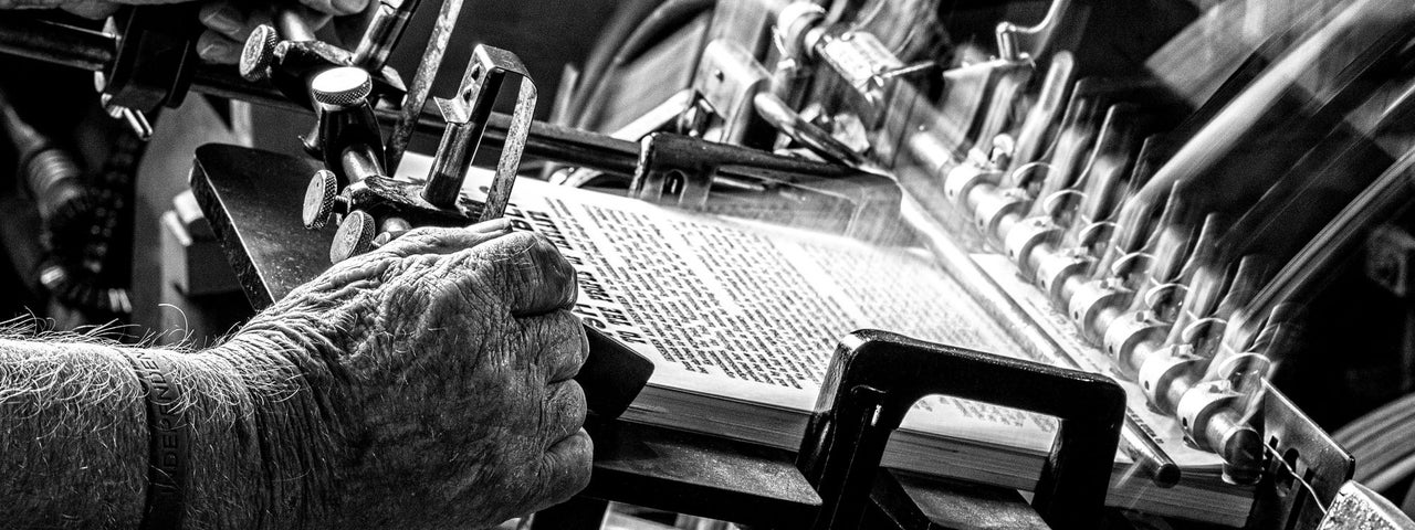 Black and white photo of hands operating old printing machine.