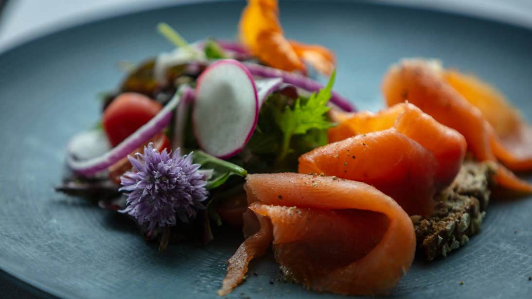 Image of smoked salmon on brown bread served on a plate garnished with salad and flowers.
