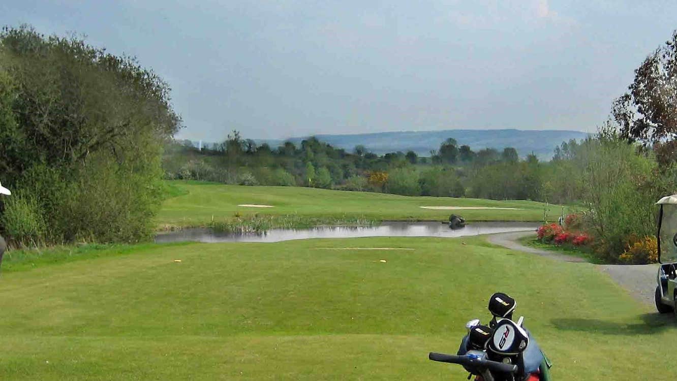 Golf clubs on a golf green with a lake two bunkers and trees in the background