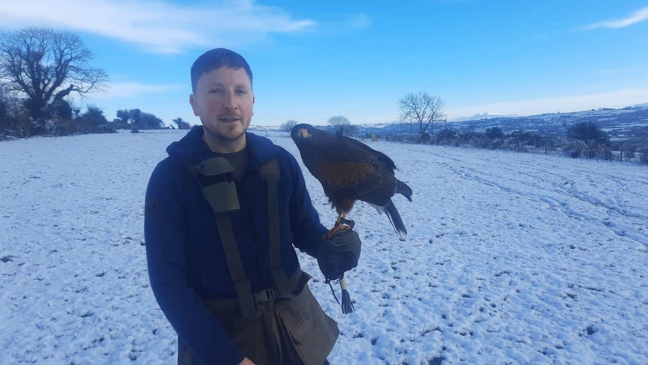 A man holding a bird of prey in a snow covered field at Faha Falconry, Killarney