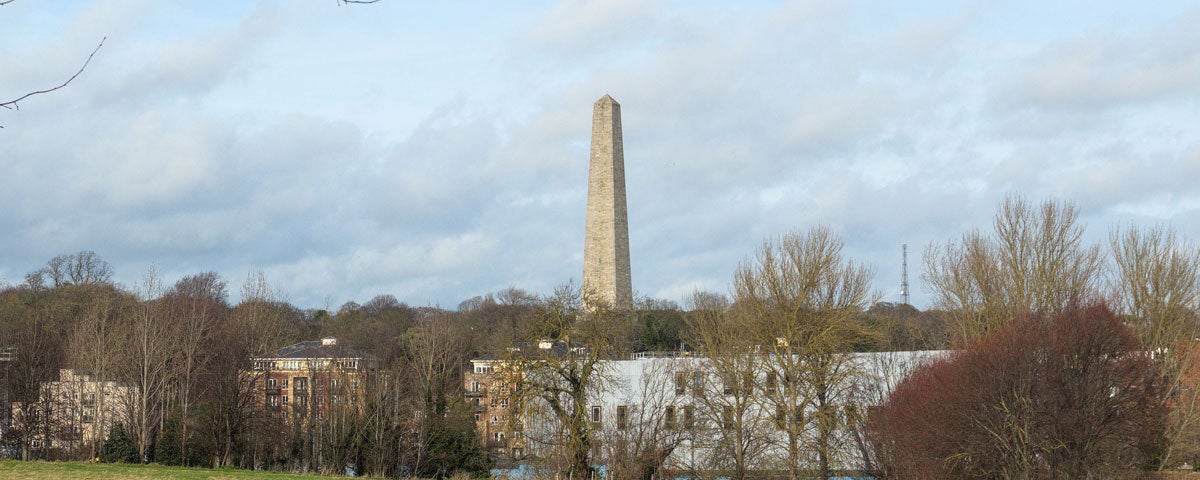 Tall stone tower with some houses and trees in foreground