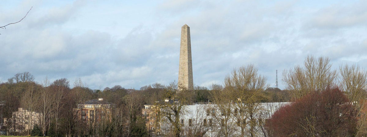 Tall stone tower with some houses and trees in foreground