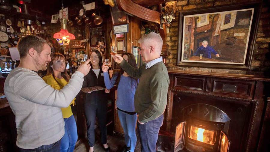 Four people tasting and toasting each other with whiskey by a pub fireside
