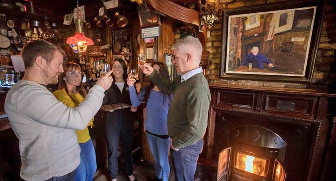 Four people tasting and toasting each other with whiskey by a pub fireside