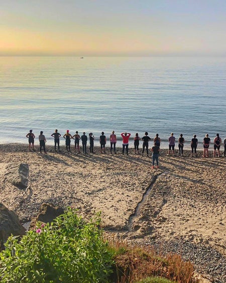 A group standing on sand by the sea watching the sunrise in the distance