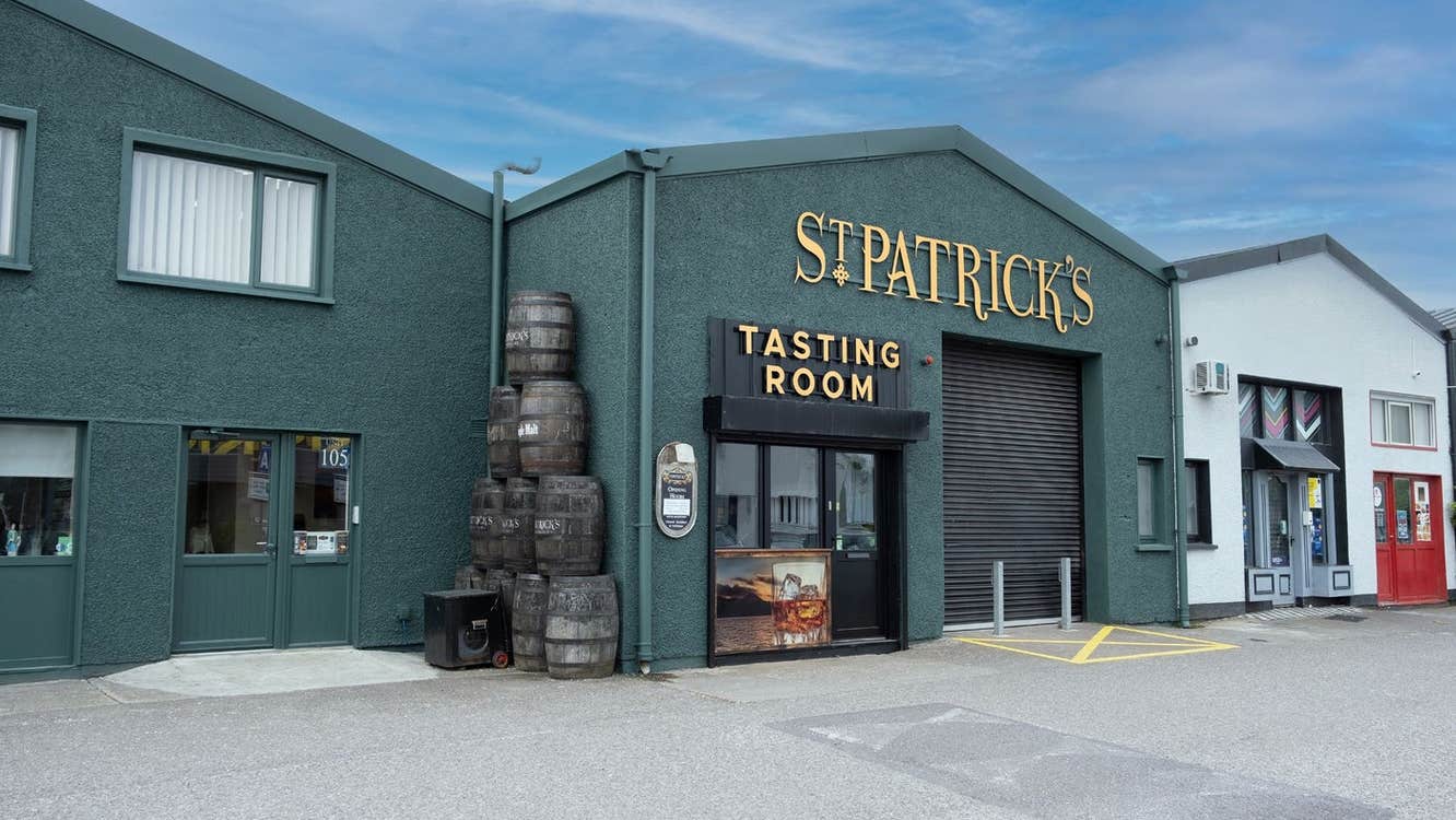 Exterior of a distillery with the name above the door and whiskey barrels on display outside