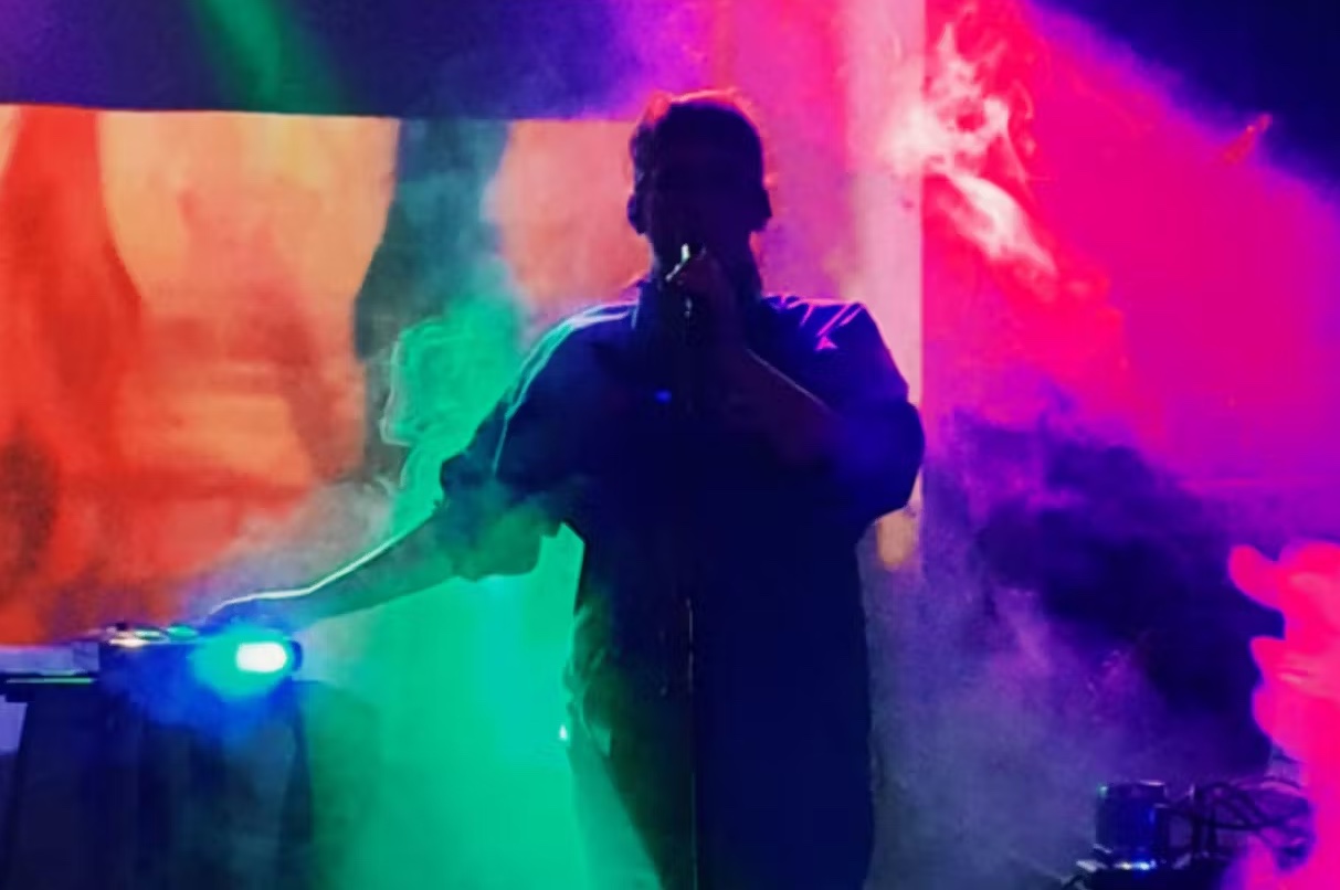 Dark silhouette of person singing with different coloured smoke swirling around them.