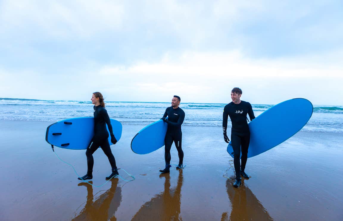 Three people walking with surfboards on Strandhill Beach in County Sligo.