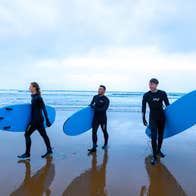 Three people walking with surfboards on Strandhill Beach in County Sligo.