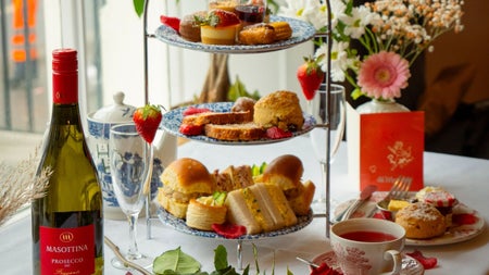 Afternoon tea stand with sandwiches cakes and scones served alongside tea prosecco and fresh flowers