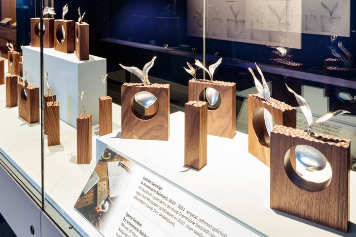 Image of a display cabinet containing small wooden blocks of different sizes with a decorative metal spoon in each one.