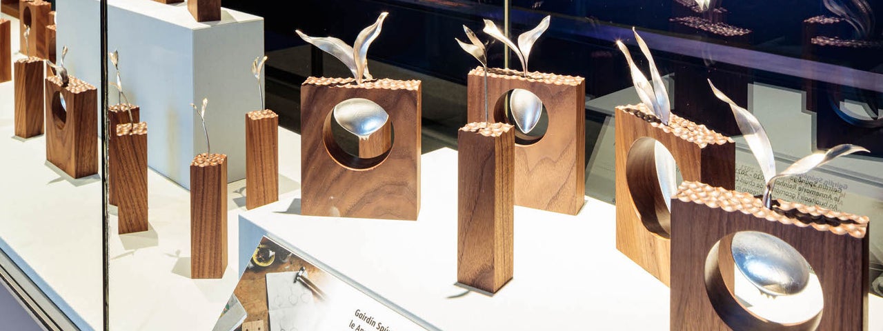 Image of a display cabinet containing small wooden blocks of different sizes with a decorative metal spoon in each one.